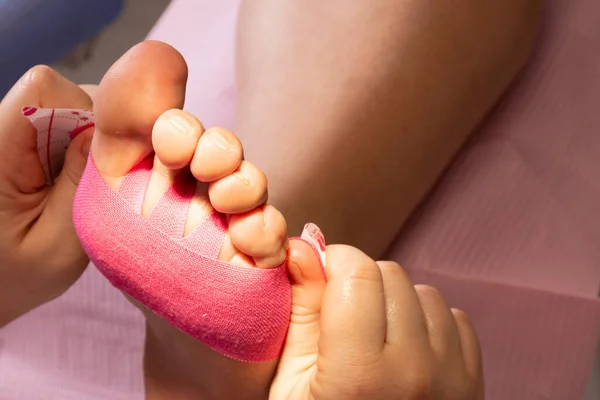 Tanımlanamayan bir ayak hastalıkları uzmanının elleri bir hastanın ayağına pembe bir Kinesio bandı yapıştırıyor.