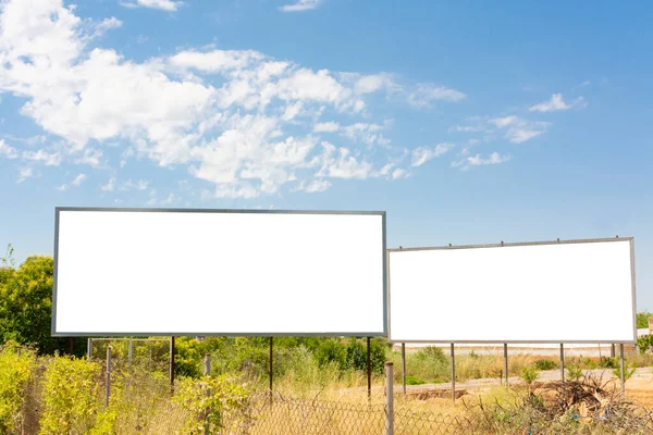 Two billboards next to a road in the field and a blue sky with clouds. Horizontal image with horizontal white copy space