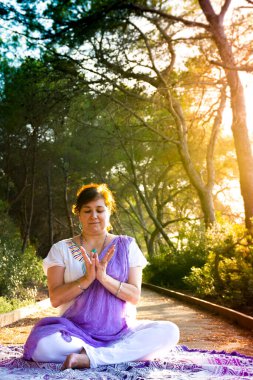 Nilüfer çiçeğinde oturmuş meditasyon yapan kadın elleriyle Lotus Mudra 'da, gün batımında ormanda bir patikada poz veriyor.