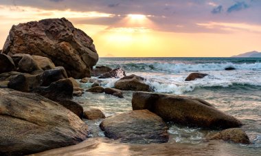 Büyük dalgalar ile denize gündoğumu. Yükselen güneş ışınlarının Bulutların arasından onların yol yapmak. Denizin üzerinde dramatik gökyüzü üzerinde fırtına bulutları. büyük taşlarla desteklemek