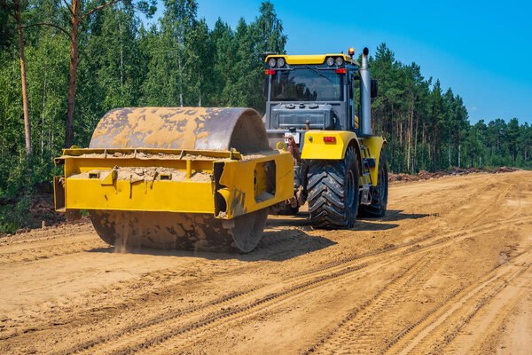 Pneumatic-tired roller compacts the soil in the embankment on the road's construction. sand consolidation on road-building. Yellow compactor driving on the sandy roadbase. soil compacting machine