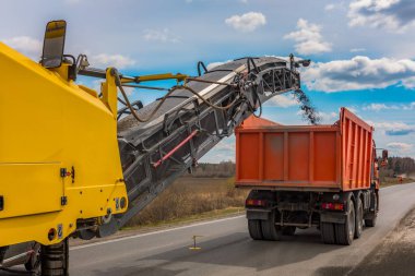 Repair of asphalt pavement of the road. Road cold milling machine removes the old asphalt and loading into a dump truck clipart