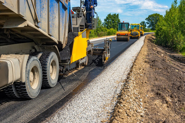 Reconstruction of the road. Dump truck unloads the asphaltic concrete mix in the paver. Roller compacts asphalt