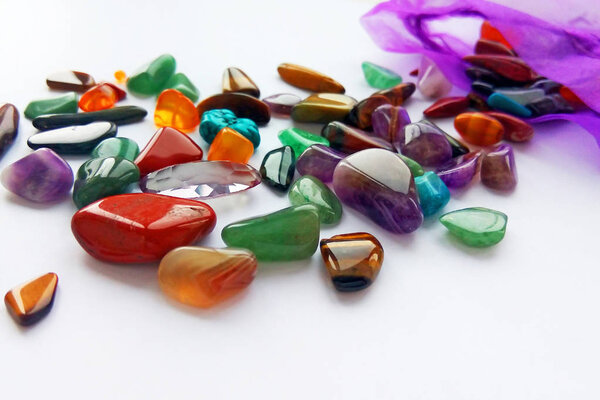 Assorted natural bright coloured semi precious gemstones and gems in bag on white background