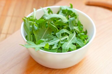 Taze sağlıklı yeşil arugula açık ahşap arka plan üzerinde beyaz bir kapta yaprakları.