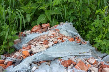 Uzak yeşil bir alanda inşaat çöp, enkaz ve atık moloz. Doğa ve toprak kirliliği konsepti