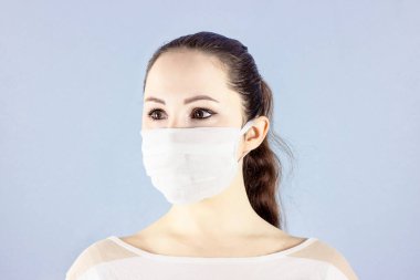 Açık mavi arka planda beyaz, tek kullanımlık tıbbi maske takan güzel beyaz kadın portresi. Virüsler ve enfeksiyon koruması, covid-19 ve 2019-ncov karantina konsepti.