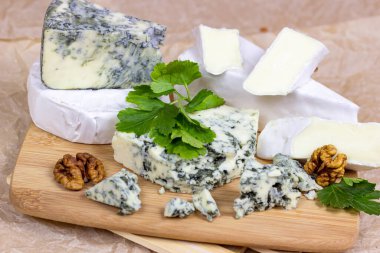 Bir çok farklı peynir çeşidi: mavi, brie peyniri, camembert ve ahşap tahta arka planda ceviz..