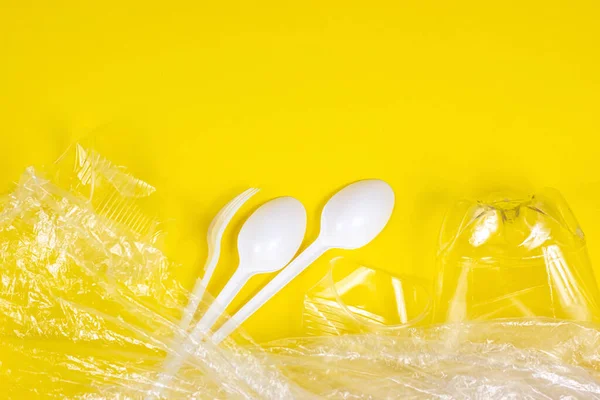 Top view of crushed plastic spoons, forks, bottles and cups as a disposable waste with copy space on bright yellow background. Environmental pollution and litter recycling concept.