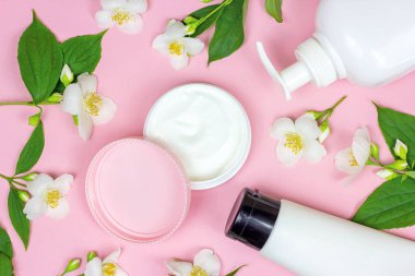 Nemlendirici krem için beyaz plastik kozmetik konteynırın üst görüntüsü açık pembe arka planda parlak taze yasemin çiçekleriyle modellenir. Vücut ve cilt bakımı, sağlık, sağlık ve güzellik konsepti.