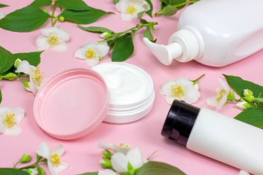 Nemlendirici krem için beyaz plastik kozmetik konteynır açık pembe arka planda parlak yasemin çiçekleri eşliğinde. Vücut ve cilt bakımı, sağlık, sağlık ve güzellik konsepti.