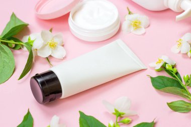 Nemlendirici krem için beyaz plastik kozmetik konteynır açık pembe arka planda parlak yasemin çiçekleri eşliğinde. Vücut ve cilt bakımı, sağlık, sağlık ve güzellik konsepti.