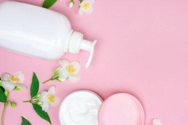 Nemlendirici krem için beyaz plastik kozmetik konteynırın en üst görüntüsü. Pembe arka planda, üzerinde fotokopi alanı olan yasemin çiçekleri olan bir model. Vücut ve cilt bakımı ve güzellik konsepti.