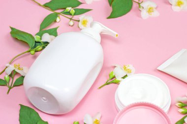 Nemlendirici krem için beyaz plastik kozmetik konteynır açık pembe arka planda parlak yasemin çiçekleri eşliğinde. Vücut ve cilt bakımı, sağlık, sağlık ve güzellik konsepti.