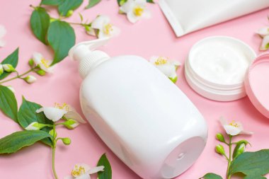 Nemlendirici krem için beyaz plastik kozmetik konteynır açık pembe arka planda parlak yasemin çiçekleri eşliğinde. Vücut ve cilt bakımı, sağlık, sağlık ve güzellik konsepti.