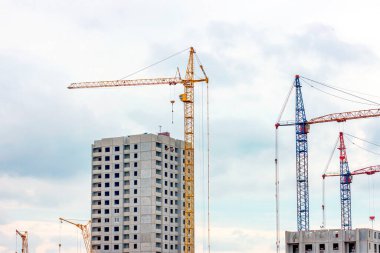 İnşaat alanında, yüksek vinçler şehirde gri bir blok ev inşa ediyor..