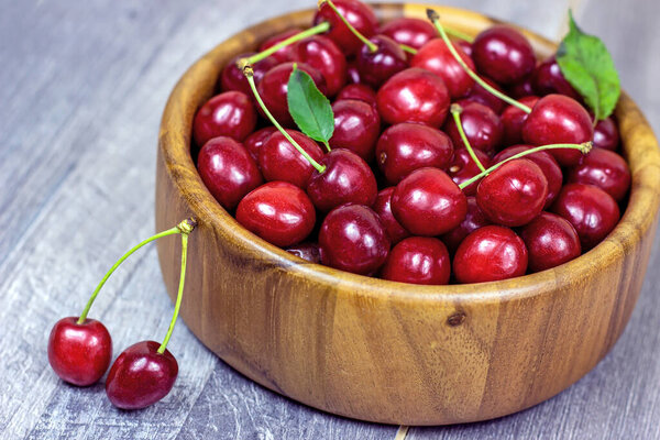 Fresh juicy red sweet cherry berries in the wooden bowl on light background in summer.