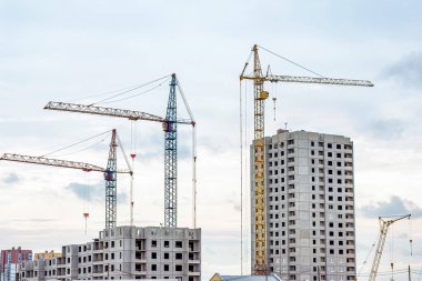İnşaat alanında, yüksek vinçler şehirde gri bir blok ev inşa ediyor..