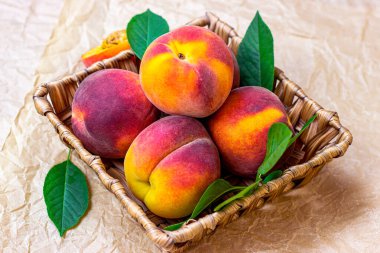 Yaz mevsiminde masa arkaplanındaki ahşap sepetin içinde taze kırmızı, sarı ve turuncu şeftaliler..