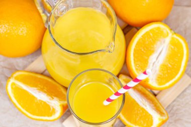 Bardaktaki taze portakal suyunun en üst görüntüsü, pipet ve kavanozla birlikte hafif ahşap arka planda meyve parçaları..