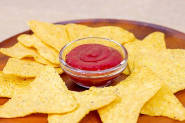 Sarı, tuzlu, çıtır çıtır ve gevrek üçgen Meksika mısır cipsleri. Hafif ahşap arka planda soslu..