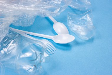 Plastik kaşıklar, çatallar ve bardaklar parlak mavi arka planda fotokopi alanı olan tek kullanımlık atıklar. Çevre kirliliği ve çöp geri dönüşümü kavramı.