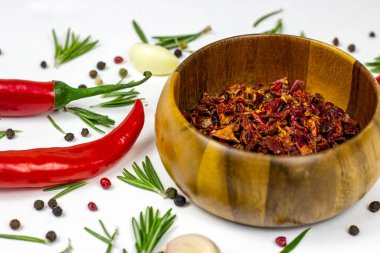 Kuru kırmızı biber dilimleri yuvarlak ahşap bir kasede, biberli, sarımsaklı ve biberiyeli beyaz gıda arka planında..