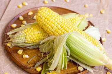 Taze pişmemiş sarı tatlı mısır, yeşil yapraklar ve tohumlarla yaz ve sonbahar mevsimlerinde ahşap arka planda..