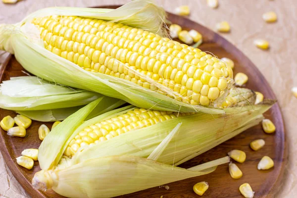 Taze pişmemiş sarı tatlı mısır, yeşil yapraklar ve tohumlarla yaz ve sonbahar mevsimlerinde ahşap arka planda..