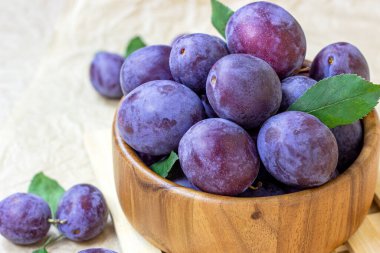Taze çiğ mavi ve menekşe erikleri ahşap kasede yeşil yapraklı arka planda.