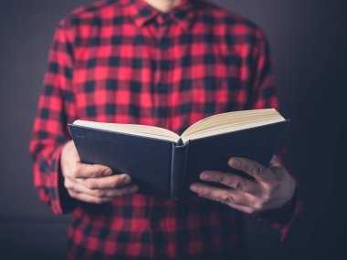 Bir pazen gömlek giymiş genç bir adam kitap okuyor