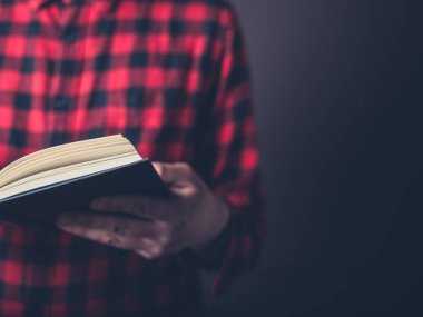 Bir pazen gömlek giymiş genç bir adam kitap okuyor