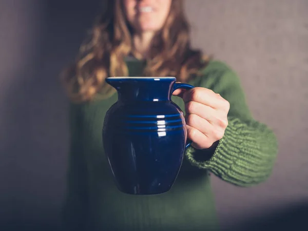 A young woman wearing a jumper is holding a ceramic jug
