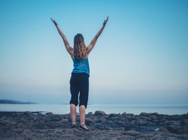 Neşeli bir kadın kollarını deniz kenarı günbatımında topluyor