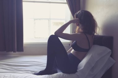 Genç bir kadın bir yatağa sabah çamaşırının içine oturuyor