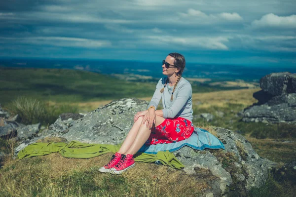 一个年轻的女人正坐在荒原上的一块岩石上 — 图库照片