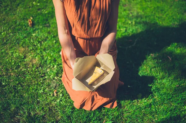 一个年轻的女人坐在草地上 盒子里有一块蛋糕 — 图库照片