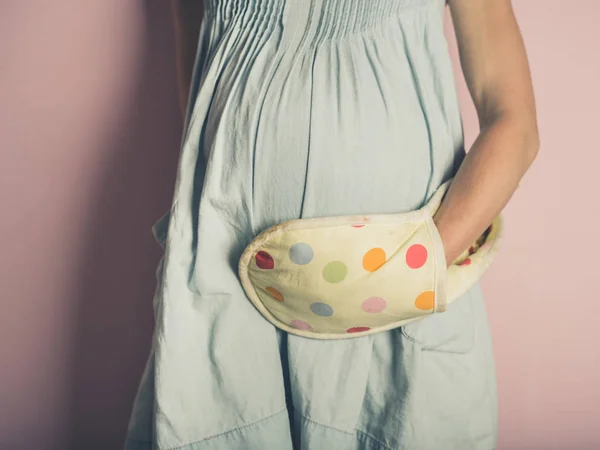 一名戴着烤箱手套的孕妇正在摸她的肚子 — 图库照片