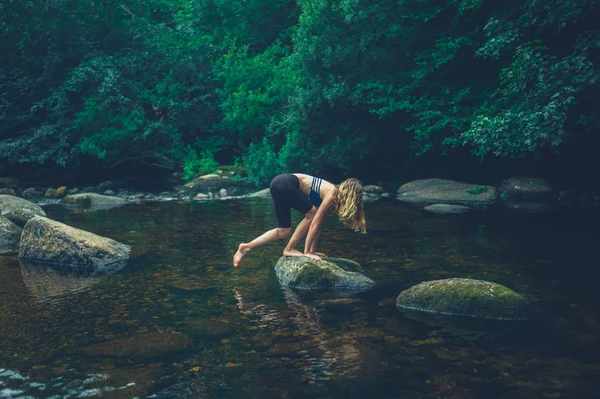 一个年轻的女人正在河里爬到一块岩石上 — 图库照片