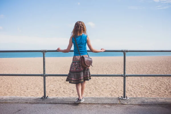 Μια Νεαρή Γυναίκα Στέκεται Ένα Κιγκλίδωμα Στην Παραλία Μια Ηλιόλουστη — Φωτογραφία Αρχείου
