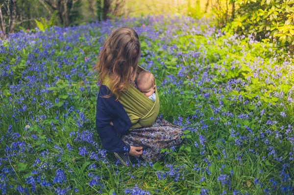 一位年轻的母亲带着一个熟睡的婴儿坐在风信子的草地上 — 图库照片