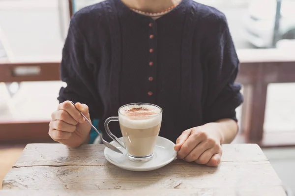 一位年轻女子正坐在咖啡馆的一张桌子旁 喝着一大杯拿铁 柴酒或类似的泡沫饮料 — 图库照片
