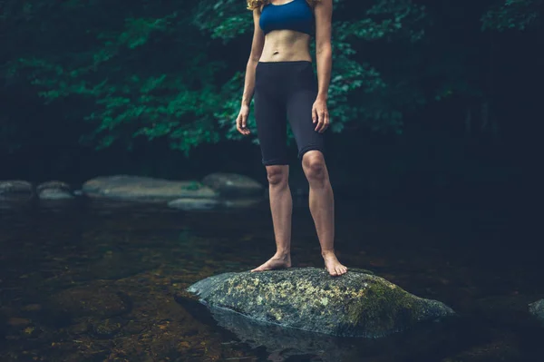 一个年轻的健身女子站在河边的一块岩石上 — 图库照片