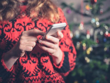 Genç bir kadın onun smartphone Noel ağacı tarafından kullanıyor