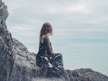 Genç bir kadın bazı kayalar denizin kenarında oturuyor