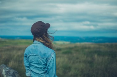 Beysbol şapkası giyen genç bir kadın bir tepenin üzerinde duruyor