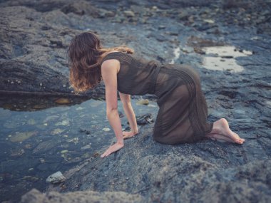 Genç bir kadın batımında sahilde bir rock havuza oturuyor