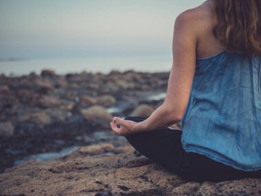 Genç kadının kırpılmış görüntü günbatımı meditasyon, denizin kenarında buzlu oturuyor