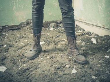 Moloz dolu bir odada ayakta Bot giyen bir gencin metrelik