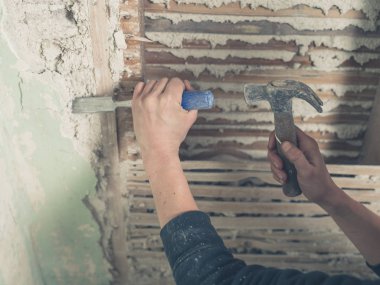 Sıva bir eski wattle and daub duvardan kaldırmak için bir çekiç kullanan bir kişi ellerinde yakın çekim